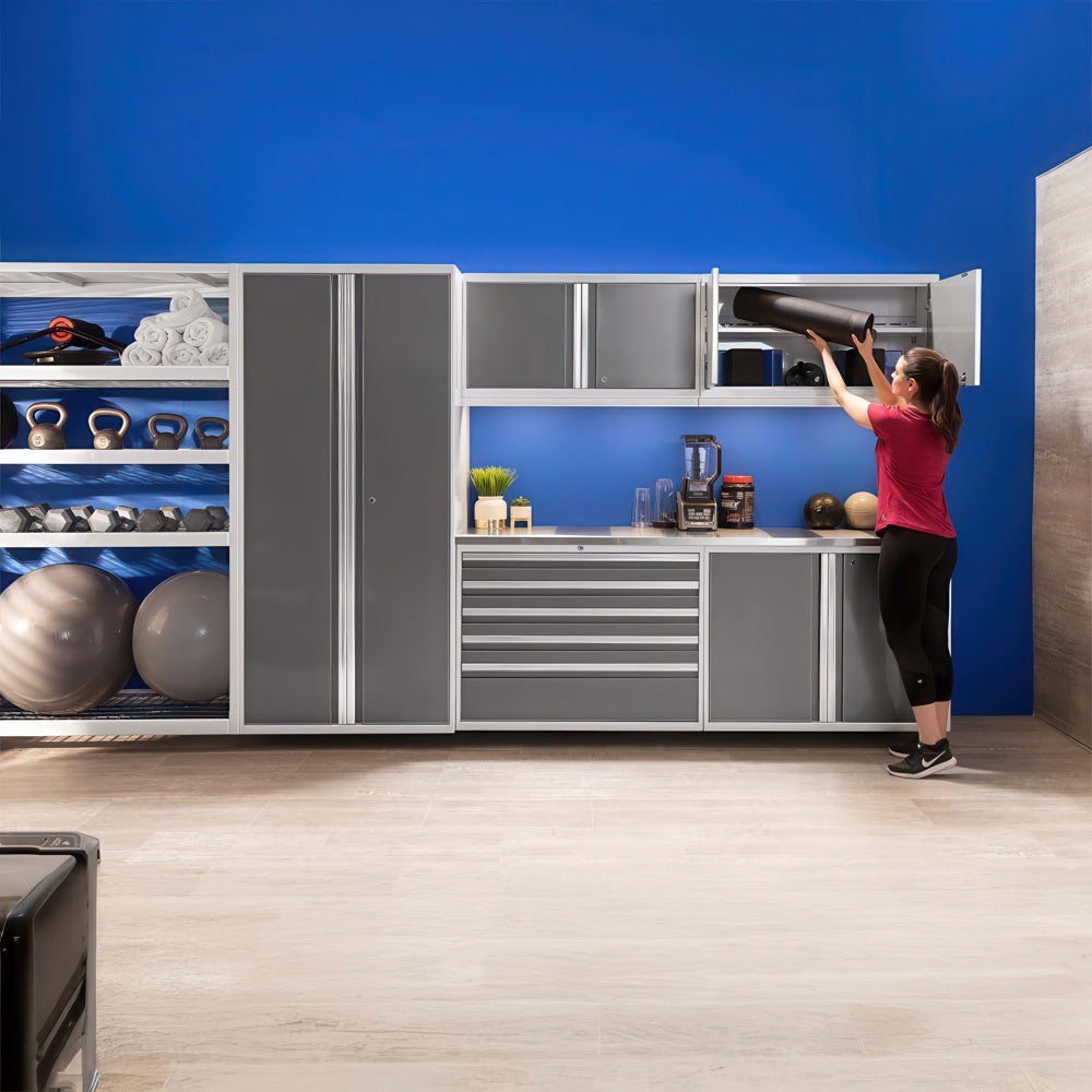 Woman Stores A Yoga Mat In Overhead Gym Cabinets In A Modern Home Fitness Space With Gray Storage And A Bright Blue Wall